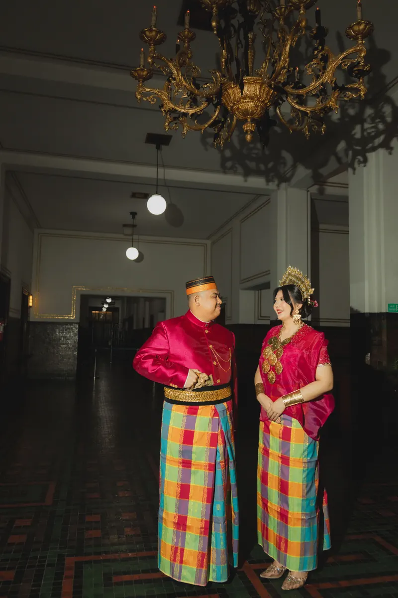 Rafli dan Dita di aula kolonial yang temaram, di bawah lampu gantung kristal