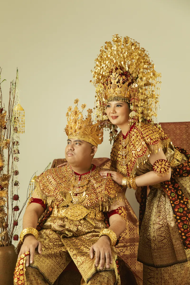 Rafli duduk dan Dita di sampingnya dalam Aesan Gede keemasan, lengkap dengan mahkota dan songket