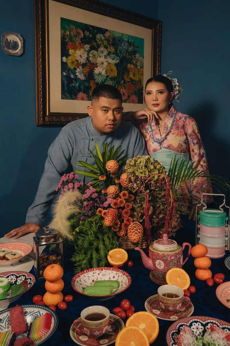 Rafli dan Dita di balik meja penuh buah, bunga, dan porselen Peranakan di ruang makan biru